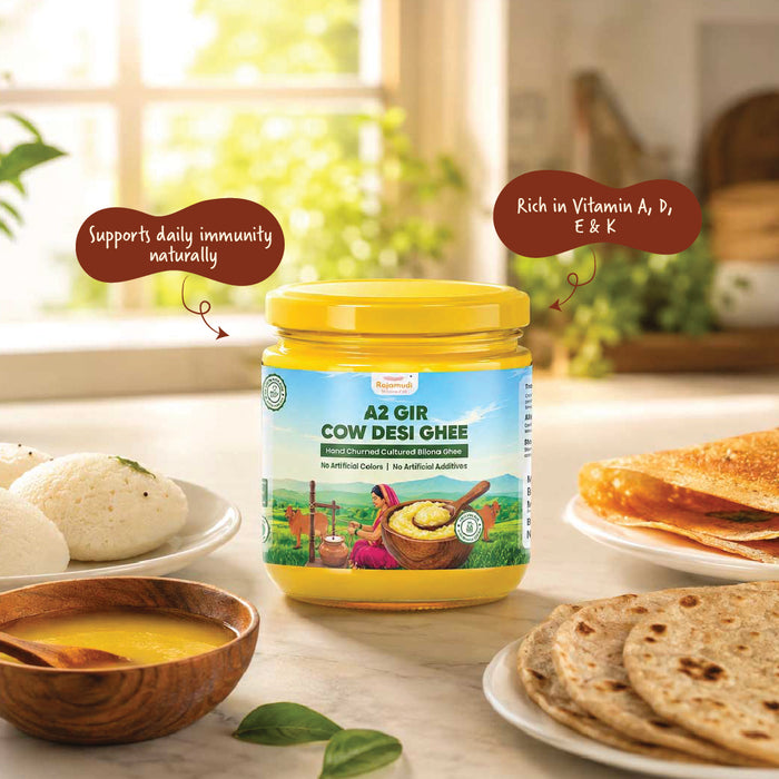 A jar of A2 Gir Cow Desi Ghee is displayed on a kitchen counter surrounded by food props like flatbread, dosas, and a bowl of yellow ghee, with two brown callout bubbles highlighting product benefits.